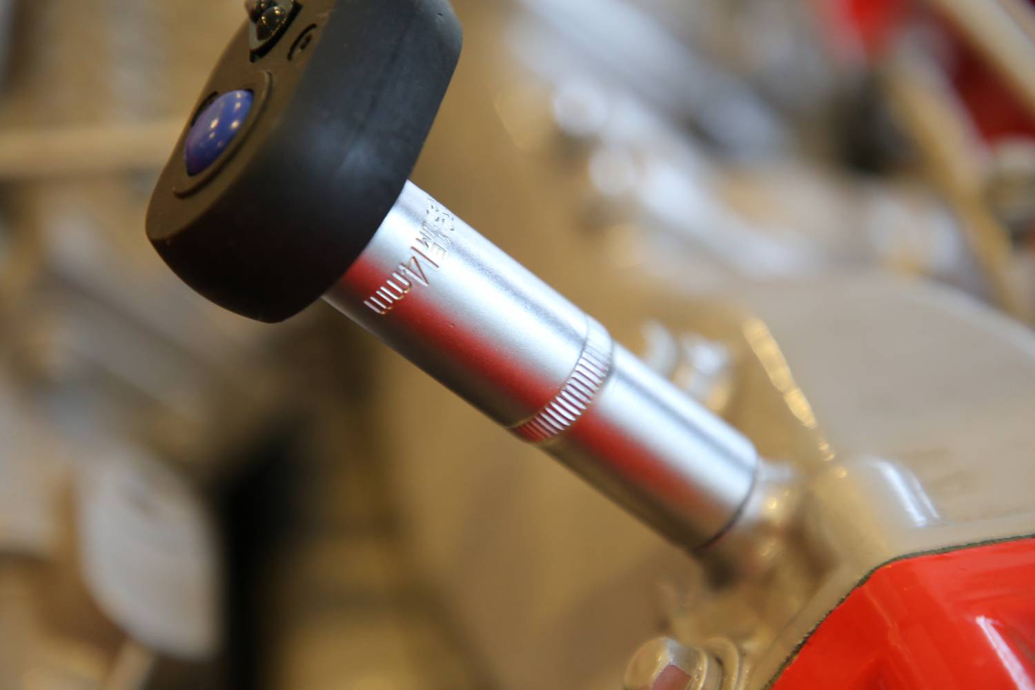 Nahaufnahme eines Metallstabs mit schwarzem Kunststoffgriff, Teil eines mechanischen Geräts, unscharfer Hintergrund.