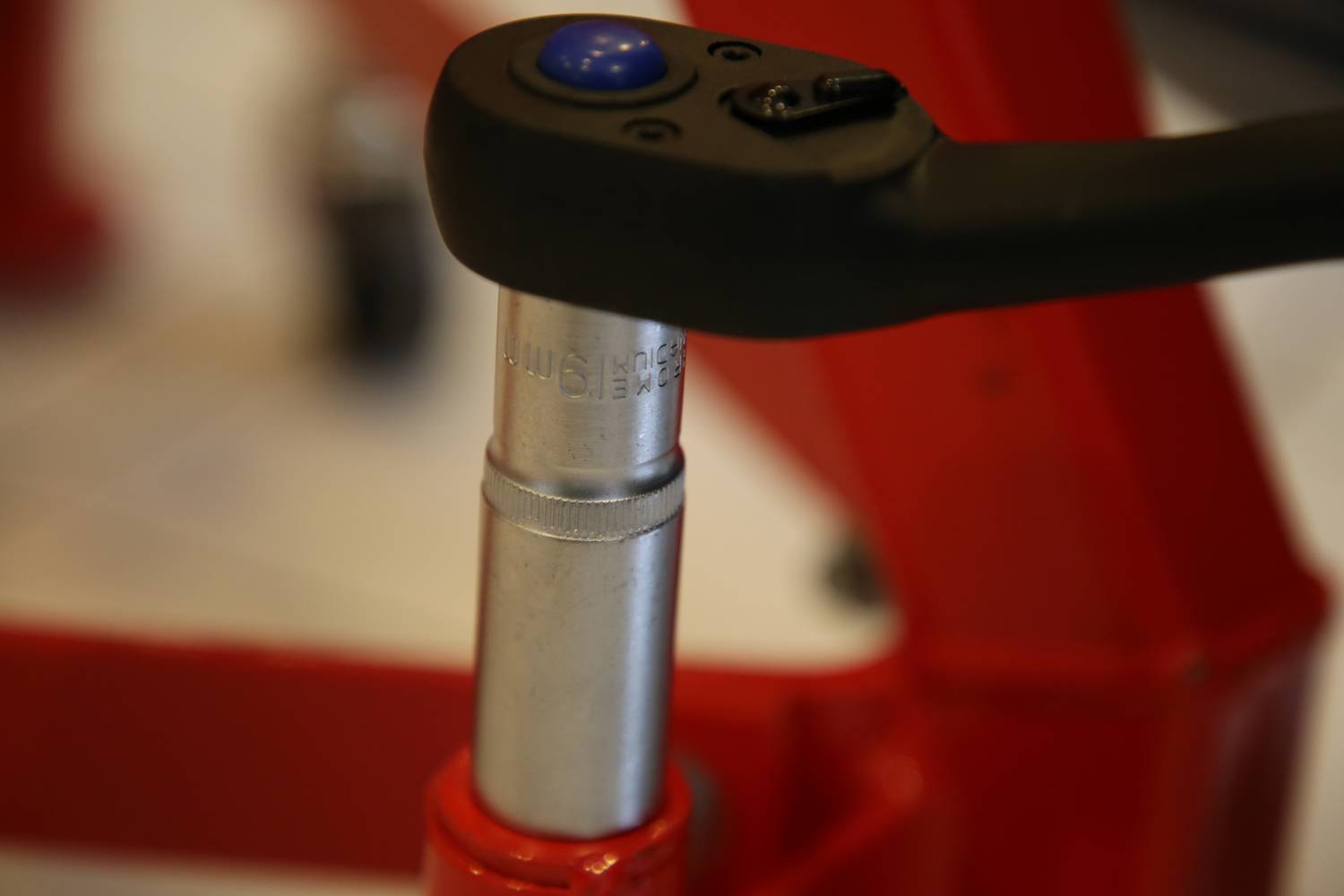 Nahaufnahme eines Metallhebels mit einer blauen Taste, befestigt an einer roten Maschine, möglicherweise Teil eines hydraulischen Wagenhebers.