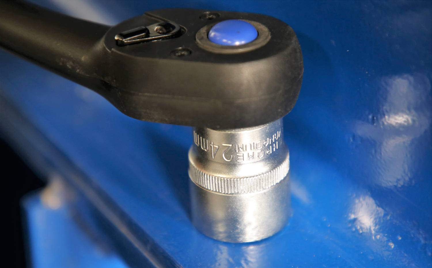 Eine Ratsche mit schwarzem Griff und blauer Taste greift eine 21-mm-Nuss, die auf einer blauen Oberfläche befestigt ist.