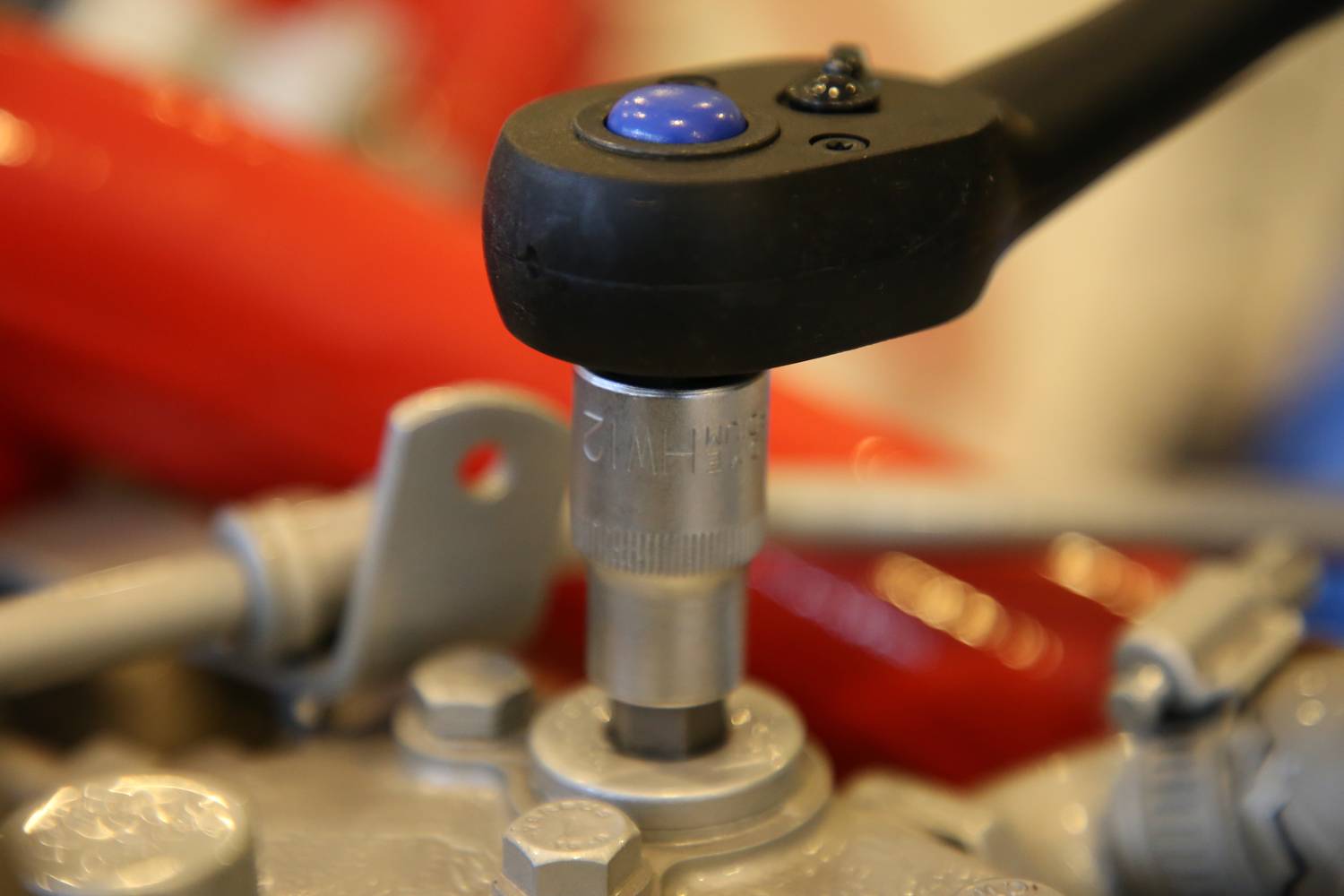 Nahaufnahme eines Schraubenschlüssels, der an einer Mutter arbeitet. Im Hintergrund sind rote Kabel sichtbar.