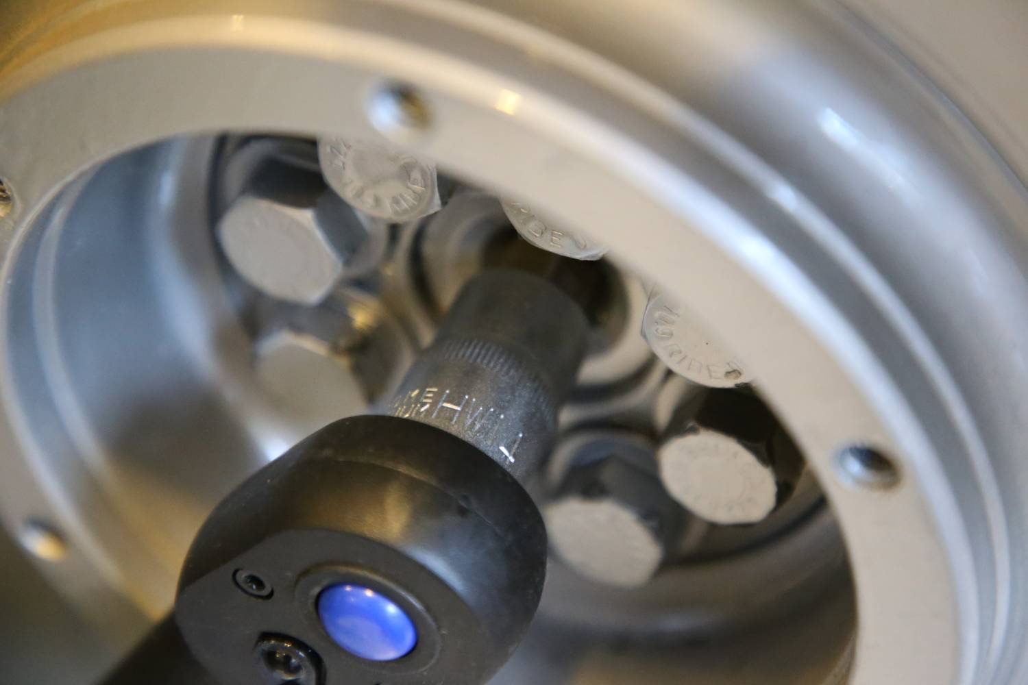 Nahaufnahme eines Schraubenschlüssels, der an einer silbernen Maschinenschraube arbeitet. Fokussiert auf mechanische Details.