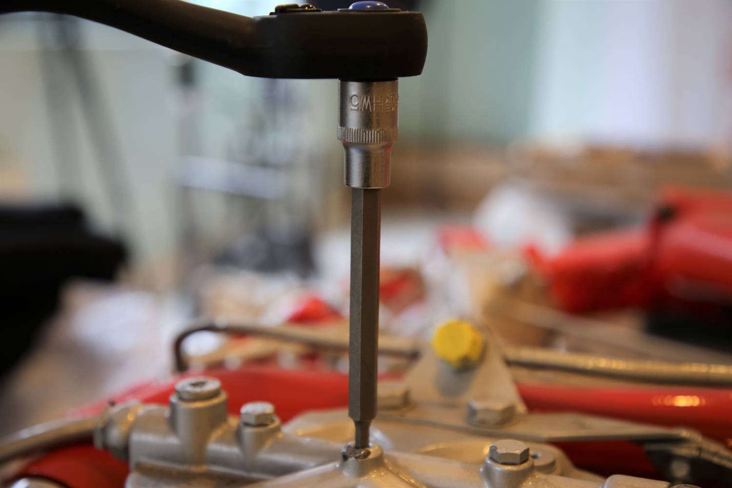 Ein Kreuzgelenk wird mit einem Schraubenschlüssel angezogen. Im Hintergrund ist verschwommenes Werkstattausrüstung zu sehen.