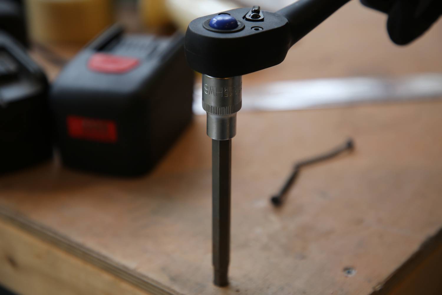 Bohrmaschine auf einer Werkbank mit Fokus auf den Bohrkopf. Im Hintergrund sind unscharfe Werkzeuge sichtbar.