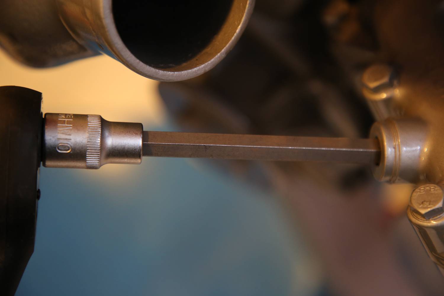 Nahaufnahme einer Ratsche mit Steckschlüssel, die an einer Maschine oder einem Fahrzeug arbeitet, wahrscheinlich für Wartungs- oder Reparaturarbeiten.