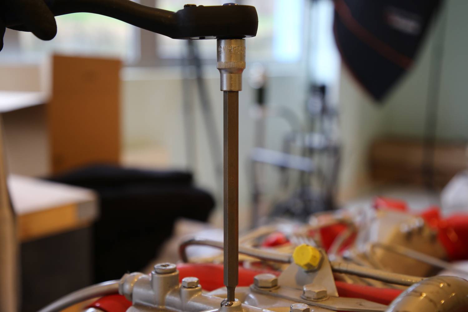 Eine Person zieht mit einem Schraubenschlüssel eine Schraube an einer Maschine fest. Im Hintergrund verschwommene Laborumgebung.