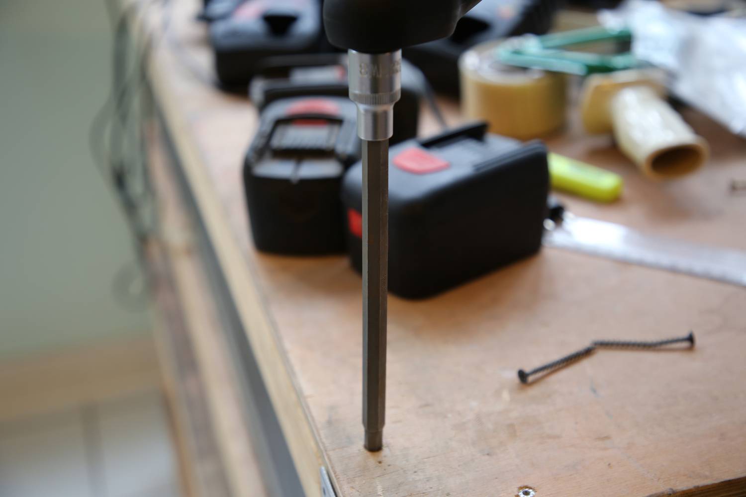 Akkuschrauber bohrt ein Loch in eine Holzoberfläche auf einer Werkbank mit Schrauben und Werkzeugen im Hintergrund.
