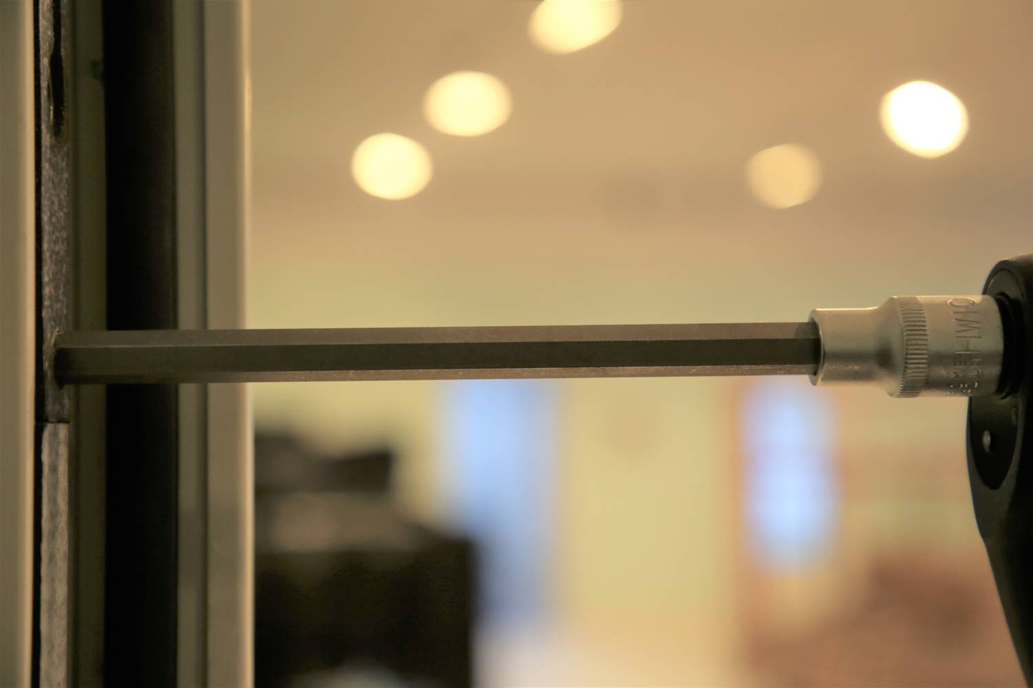 Ein Schraubendreher zieht eine Schraube in eine Metalloberfläche ein. Der Hintergrund ist unscharf und zeigt eine Innenraumszene.