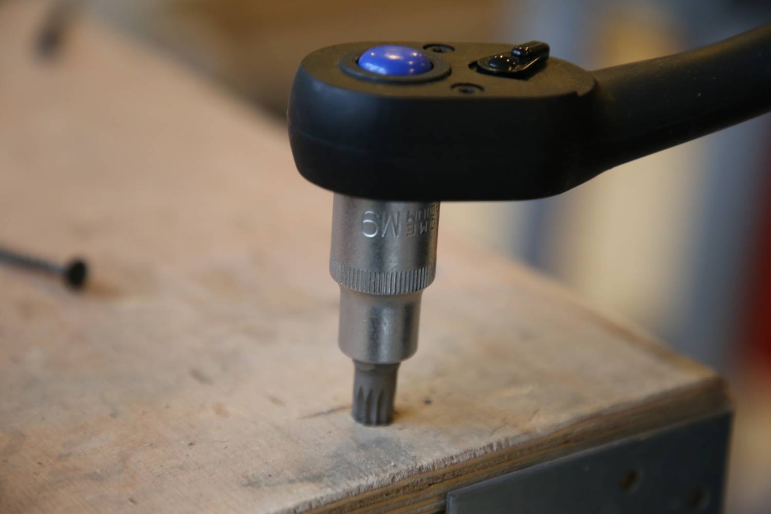 'Akkuschrauber dreht Schraube in eine Holzplatte.' Die Nahaufnahme zeigt den Schrauber beim Arbeiten auf der Oberfläche eines Holztischs.