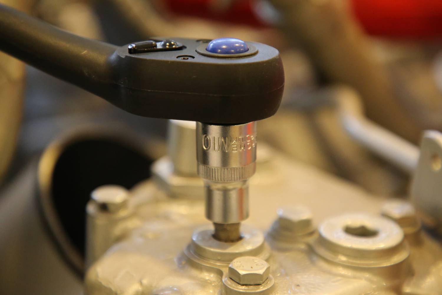 Ein Drehmomentschlüssel zieht eine Schraube an einem metallischen Gerät fest. Der Hebelgriff ist schwarz mit einem blauen Knopf.