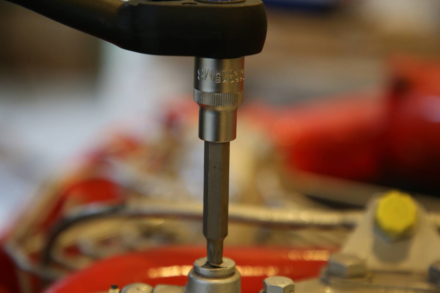 Nahaufnahme eines Schraubendrehers, der eine Schraube in ein mechanisches Bauteil mit roten und metallischen Oberflächen dreht.