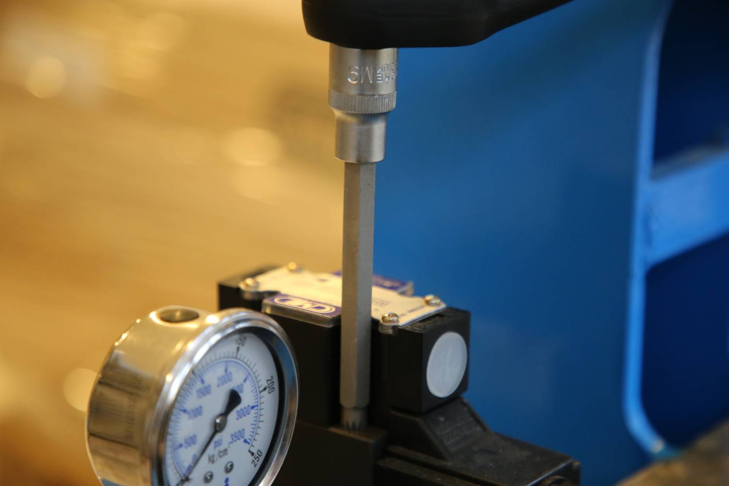 Nahaufnahme einer Maschine mit Manometer und einer Halterung, die etwas umschließt, möglicherweise Teil eines Prüfverfahrens.