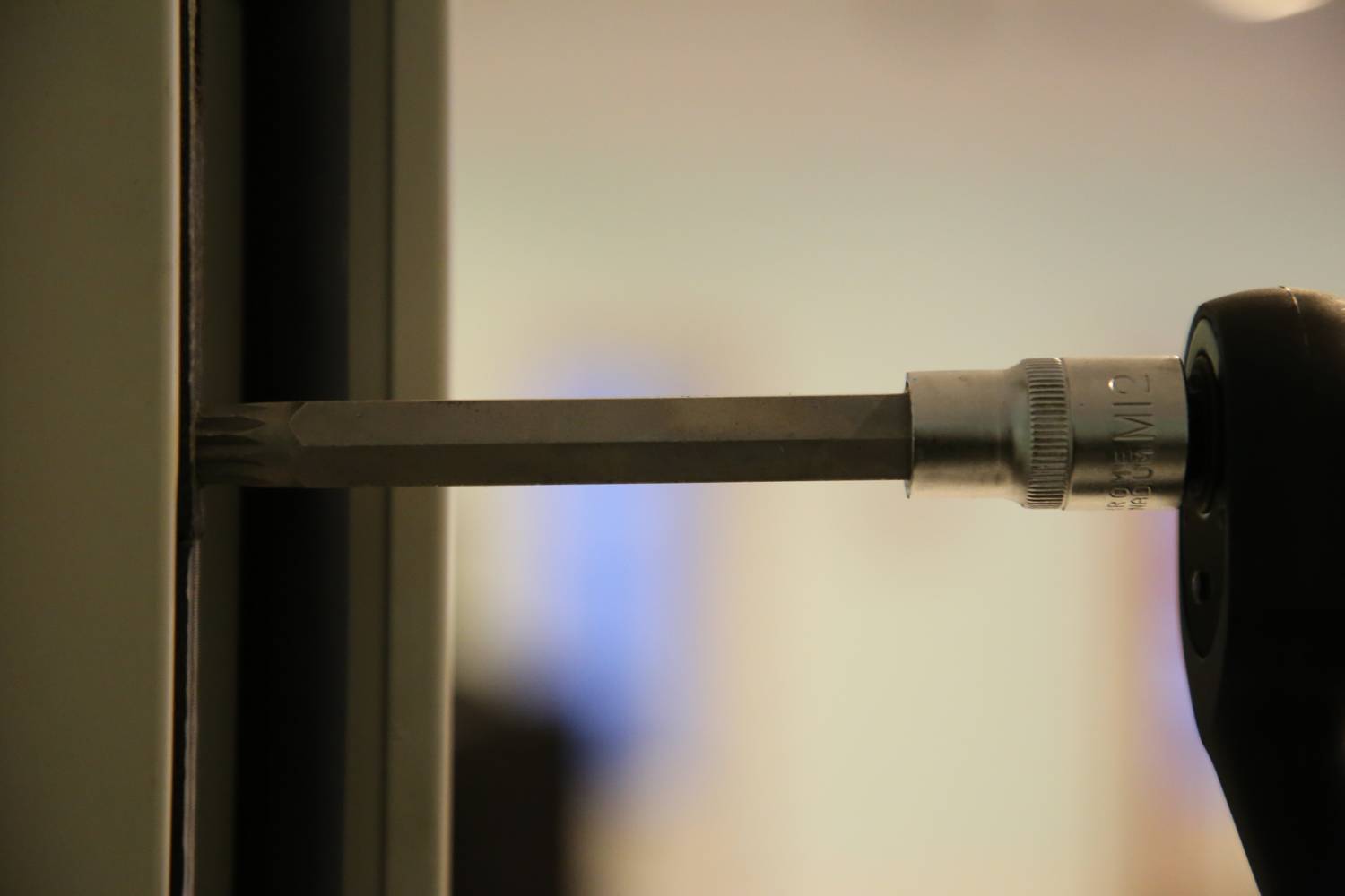 Ein Schraubendreher wird in eine Vertiefung an einem Metallrahmen eingesetzt. Details der Umgebung sind unscharf.