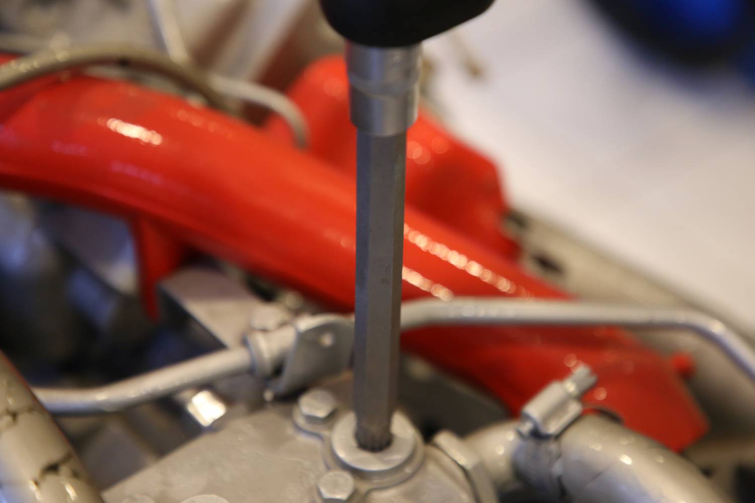 Nahaufnahme eines glänzenden Motorbauteils mit rotem Rohr und metallischen Schläuchen. Im Fokus steht ein Schraubenschlüssel.