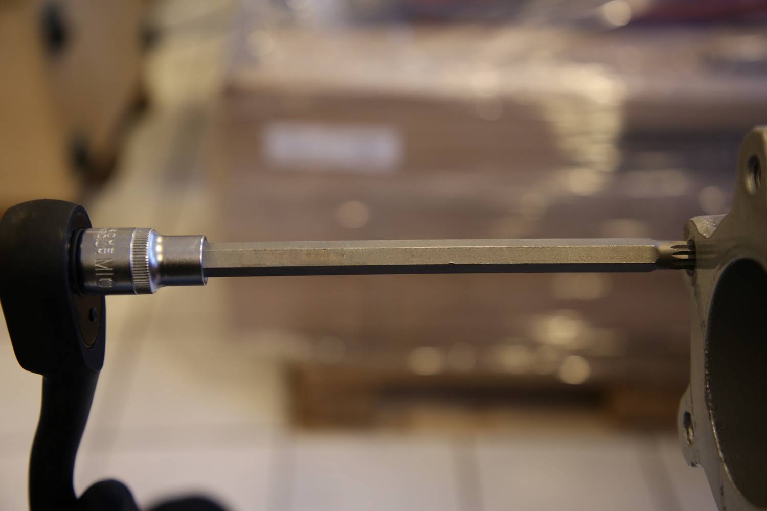 Ein langer Schraubenschlüssel, der an einem Metallgegenstand befestigt ist, mit einem verschwommenen Hintergrund aus Kisten oder Paketen.