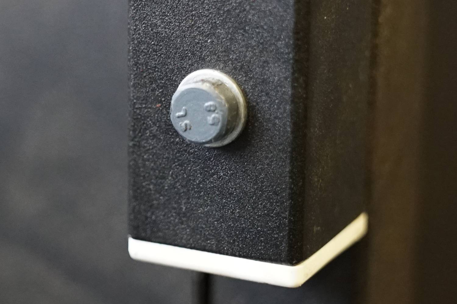 Nahaufnahme einer schwarzen Metallboxecke mit einer herausstehenden silbernen Schraube.