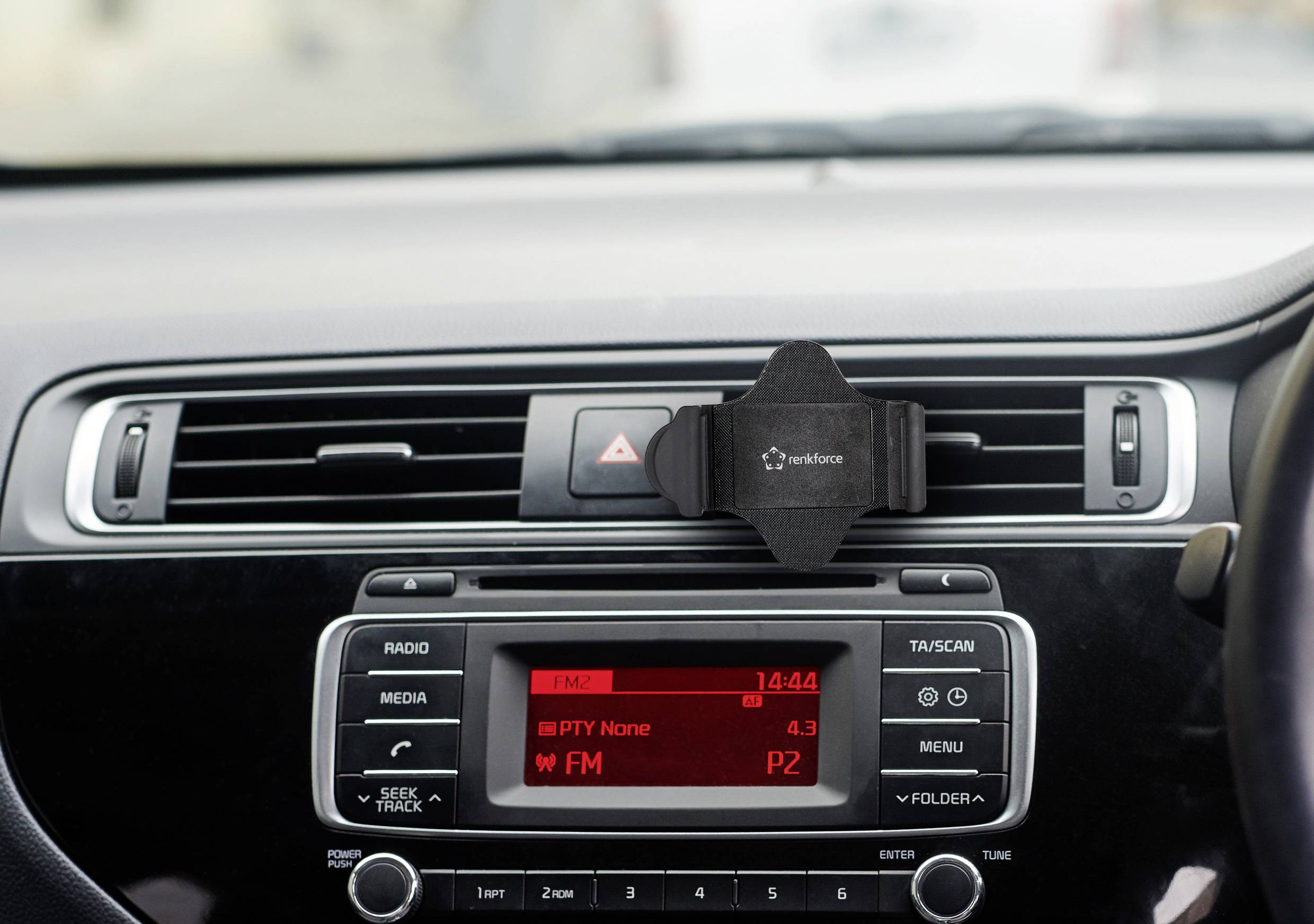 Auto-Armaturenbrett mit Radioanzeige. Zeigt Uhrzeit '14:44', FM-Radio eingeschaltet, Sender P2. Handyhalterung in Belüftungsschlitzen.