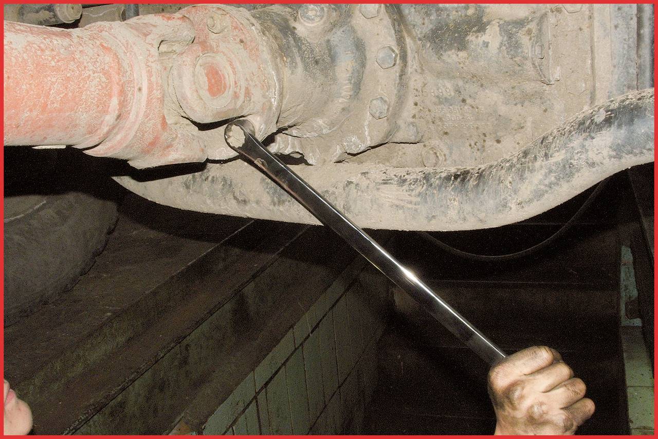 Mechaniker zieht mit Schraubenschlüssel eine Schraube am unteren Teil eines Fahrzeugs an. Der Bereich ist schmutzig und staubig.