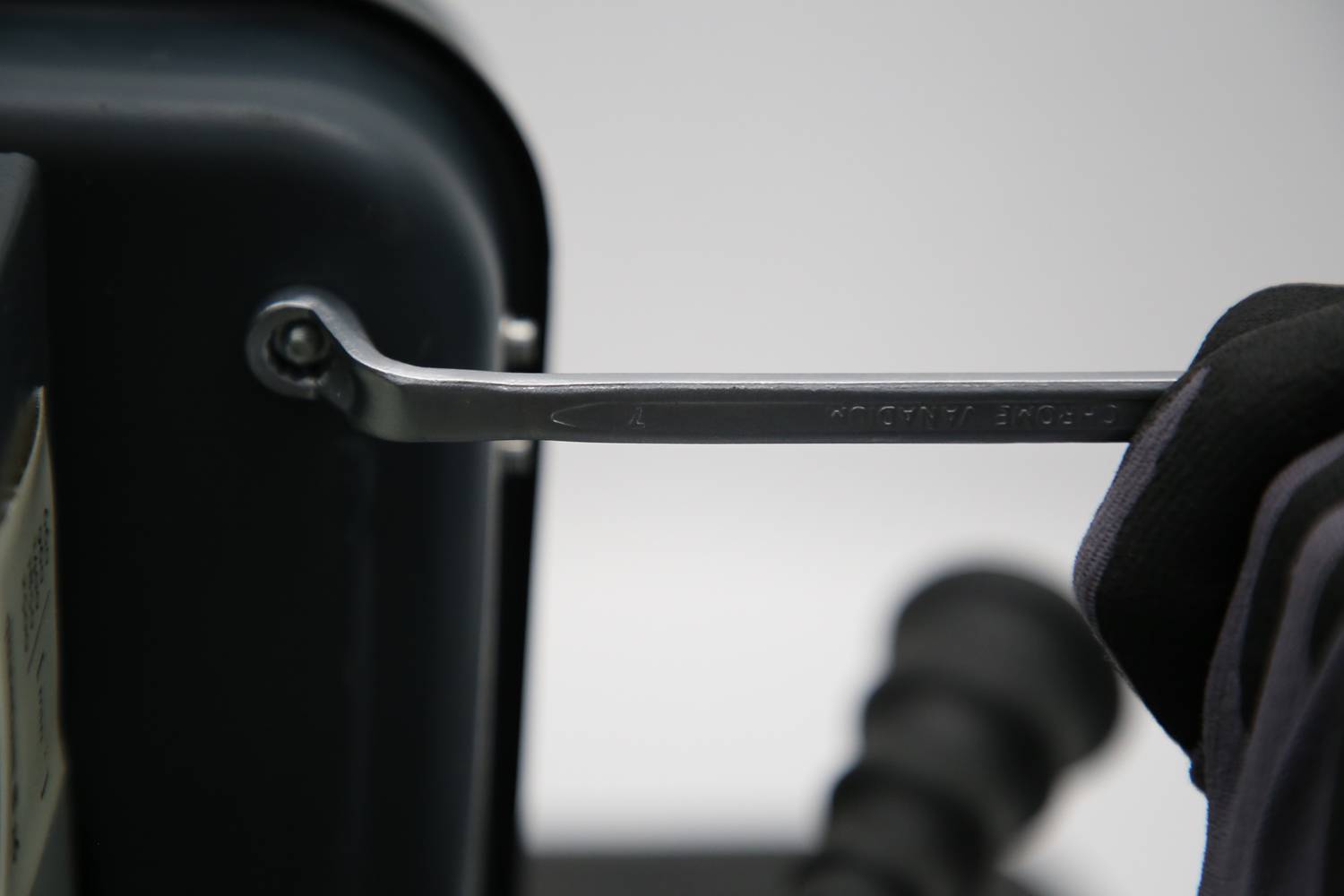 Eine Hand zieht mit einem Schraubenschlüssel eine Schraube an einem schwarzen Gerät fest.