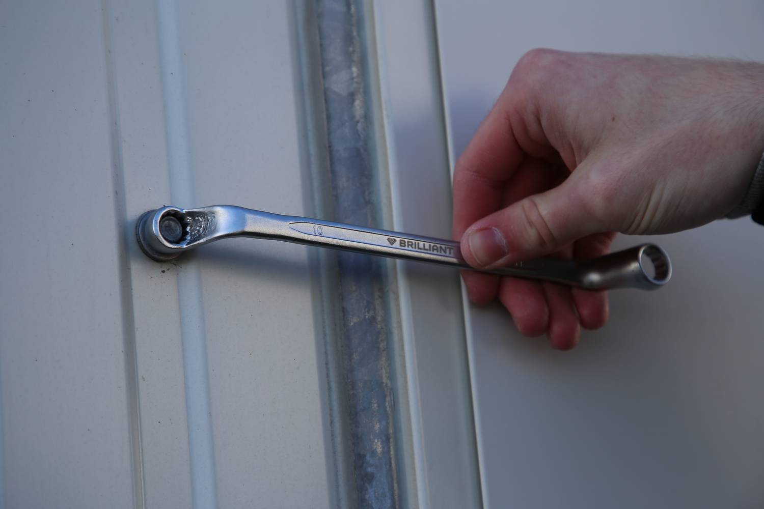 Eine Hand hält einen Schraubenschlüssel, der eine Schraube anzieht.