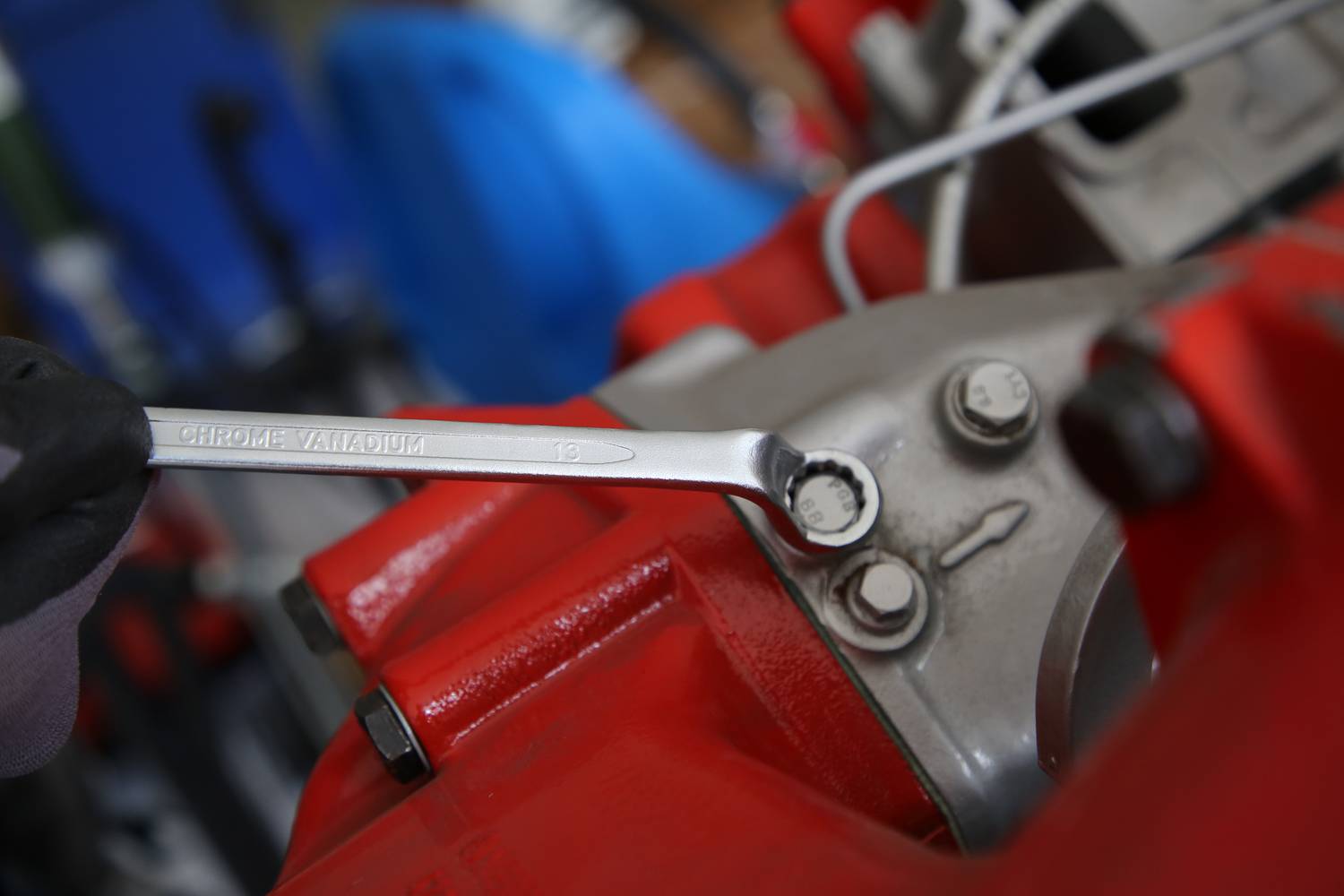 Eine Person benutzt einen Schraubenschlüssel, um eine Mutter an einem rot lackierten Maschinenbauteil festzuziehen.