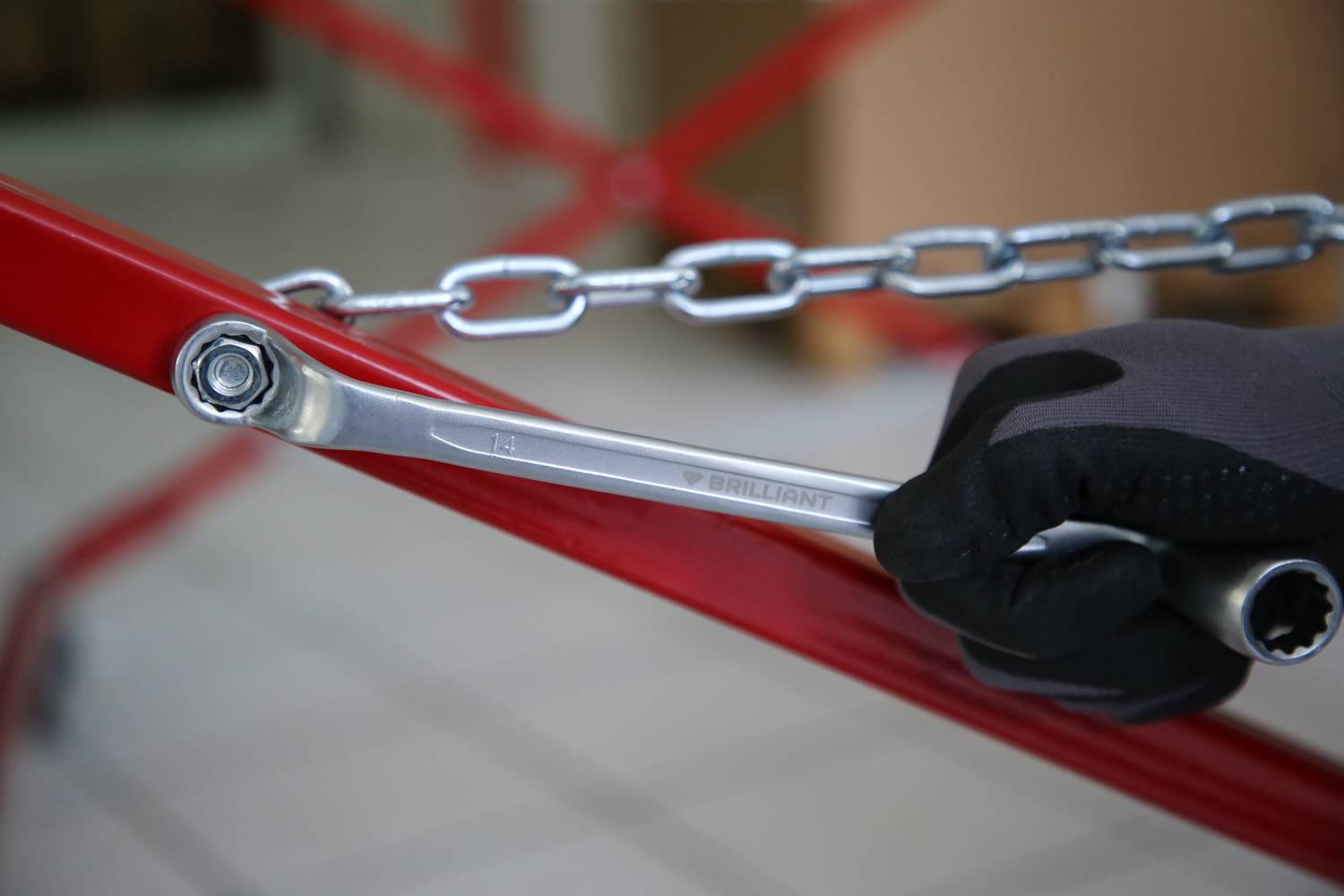 Hand in Handschuh hält einen Schraubenschlüssel, der an einer Kette angebracht ist, symbolisiert handwerkliche Arbeit oder Reparatur.