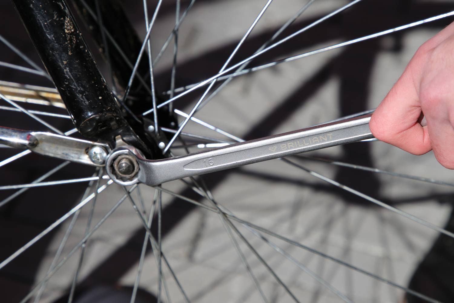 Nahaufnahme einer Person, die ein Fahrrad repariert, indem sie mit einem Schraubenschlüssel an einer Schraube am Hinterrad arbeitet.