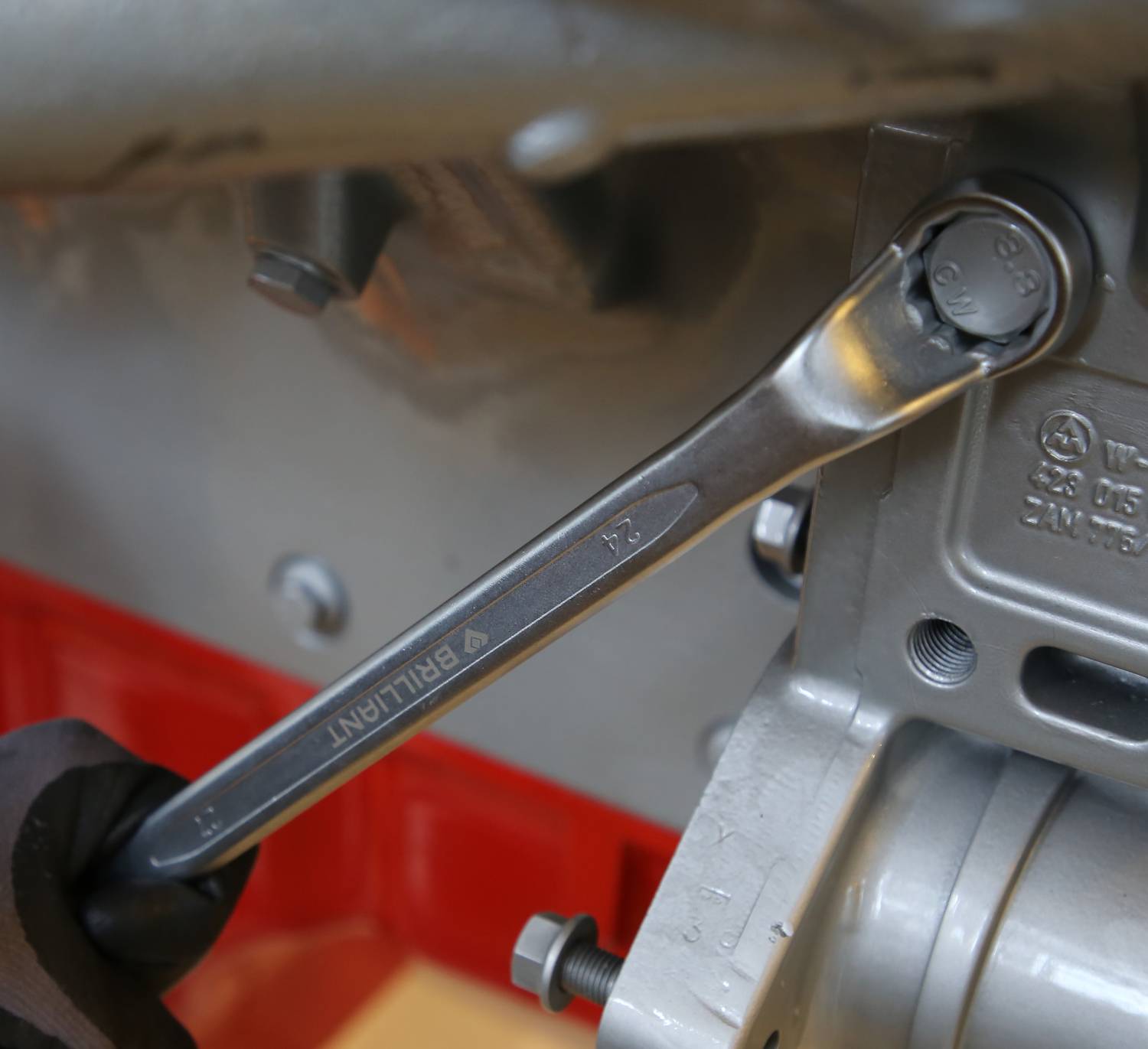 Ein Schraubenschlüssel dreht einen Bolzen an einem metallischen Bauteil in einer Werkstattumgebung.