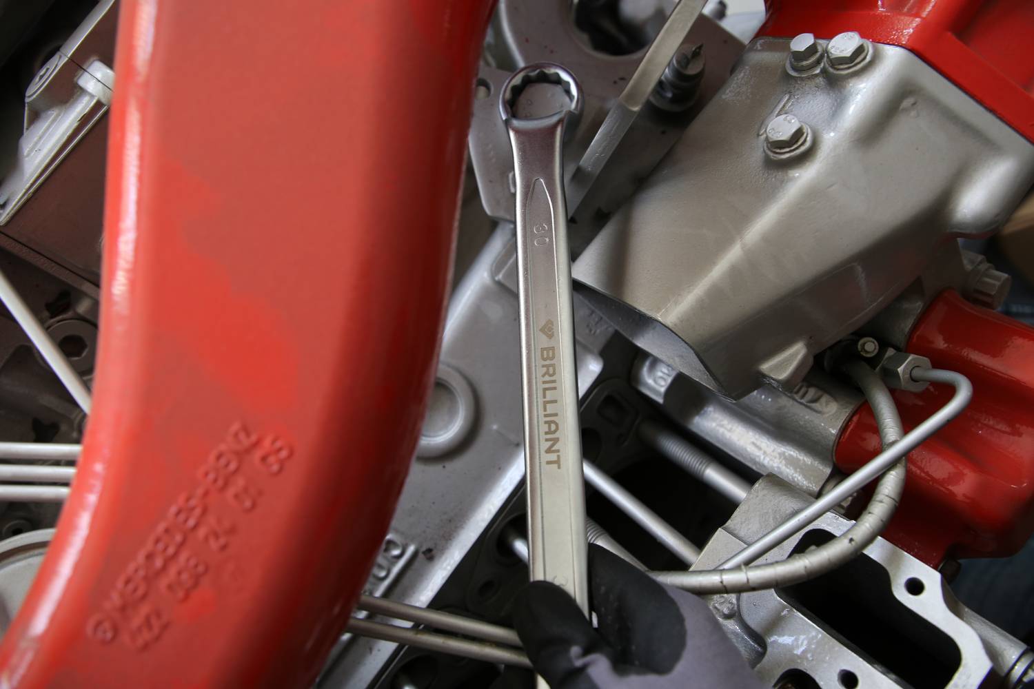 Hand hält Schraubenschlüssel an einer Maschine mit roten und silbernen Teilen. Schraubenschlüssel trägt Aufschrift 'BRILLIANT'.