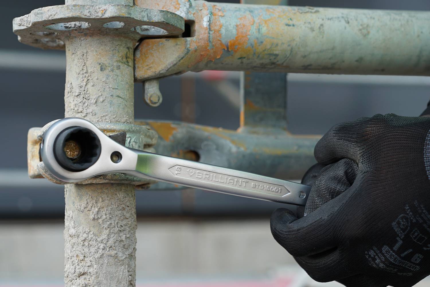 Ein Arbeiter mit schwarzen Handschuhen zieht eine Schraube an einem Metallgerüst mithilfe eines silbernen Schraubenschlüssels fest.