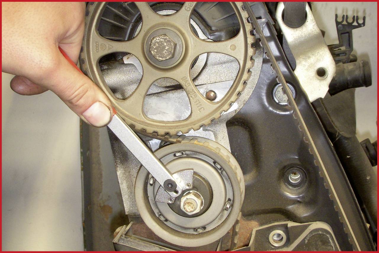 Eine Hand hält einen Schraubenschlüssel an einem Zahnriemen in einem Motorraum.