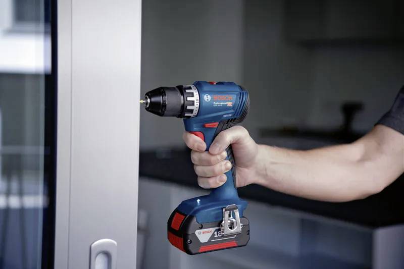 Eine Person, die eine kabellose Elektrobohrmaschine in der Nähe eines Fensters hält, was auf Heimwerker- oder Reparaturarbeiten hindeutet.