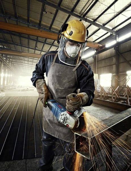 Ein Arbeiter in Schutzausrüstung verwendet ein Elektrowerkzeug, um Metall zu schneiden, während Funken sprühen, in einem großen Industrielager.