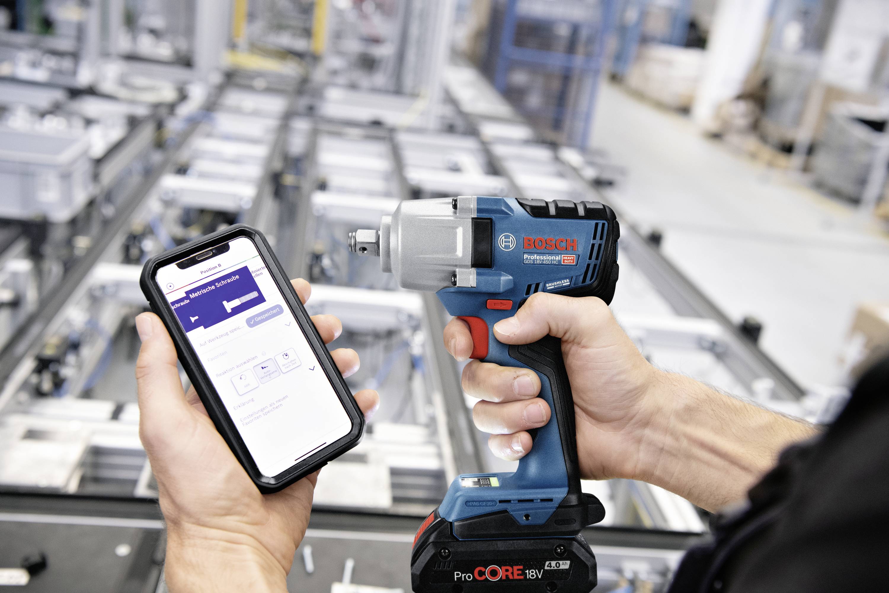 Eine Person hält ein Smartphone mit einer App neben einem Bosch Akku-Schlagschrauber in einer industriellen Umgebung.