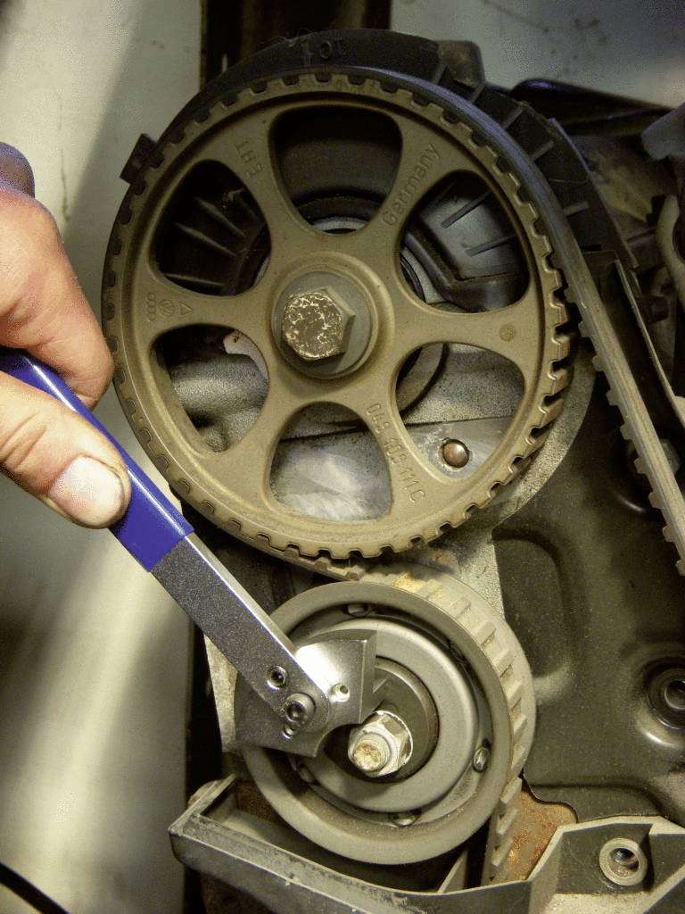 Ein Schraubenschlüssel spannt den Zahnriemen eines Motors, um die Spannung zu überprüfen und anzupassen. Der Fokus liegt auf der Wartung.