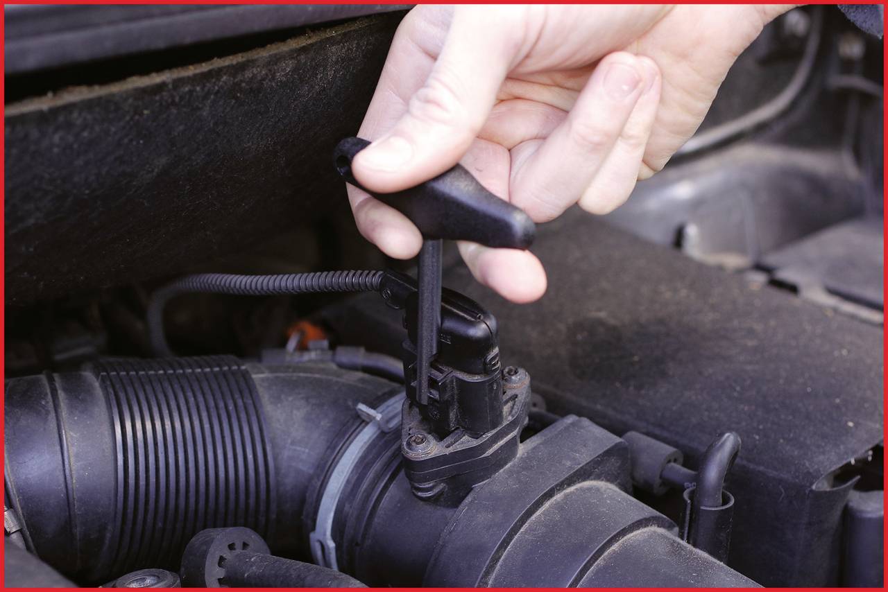 Eine Hand zieht einen Ölmessstab aus einem Auto-Motorraum, um den Ölstand zu prüfen. Der Motor weist typische Verschmutzungen auf.