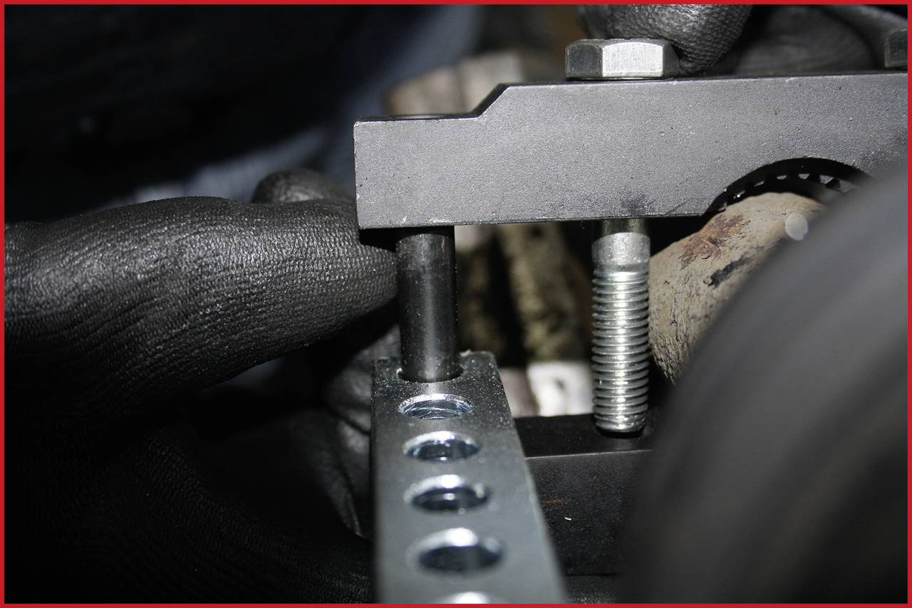 Nahaufnahme eines Metallrahmens mit Bolzen und Schrauben, gehalten von zwei schwarzen Handschuhen. Fokus auf den Zusammenbau.