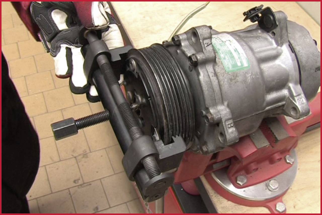 Eine Person nutzt ein Abziehwerkzeug, um ein Teil von einem silbernen Gerät, das in einem Schraubstock eingespannt ist, zu entfernen.