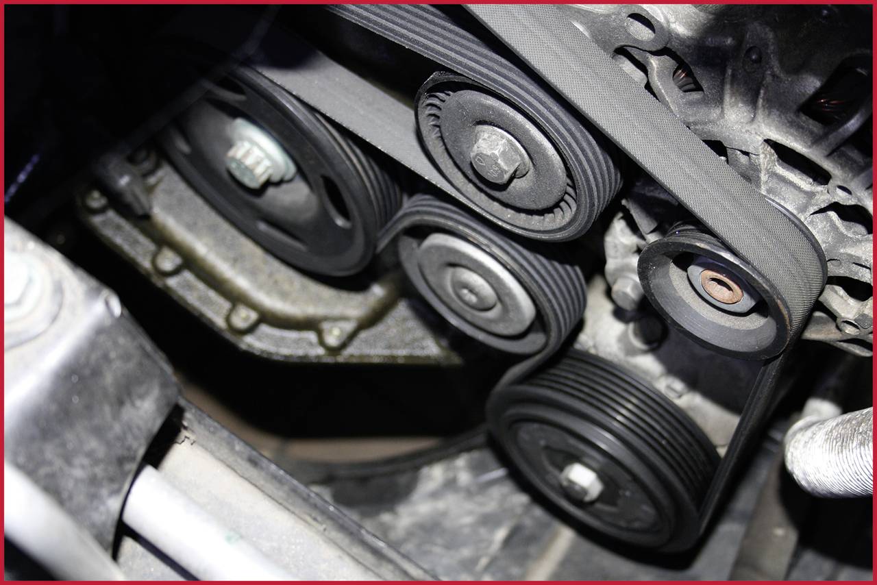 Ein Auto-Motorraum mit mehreren Riemenscheiben und einem Keilriemen, der über die Rollen gespannt ist.