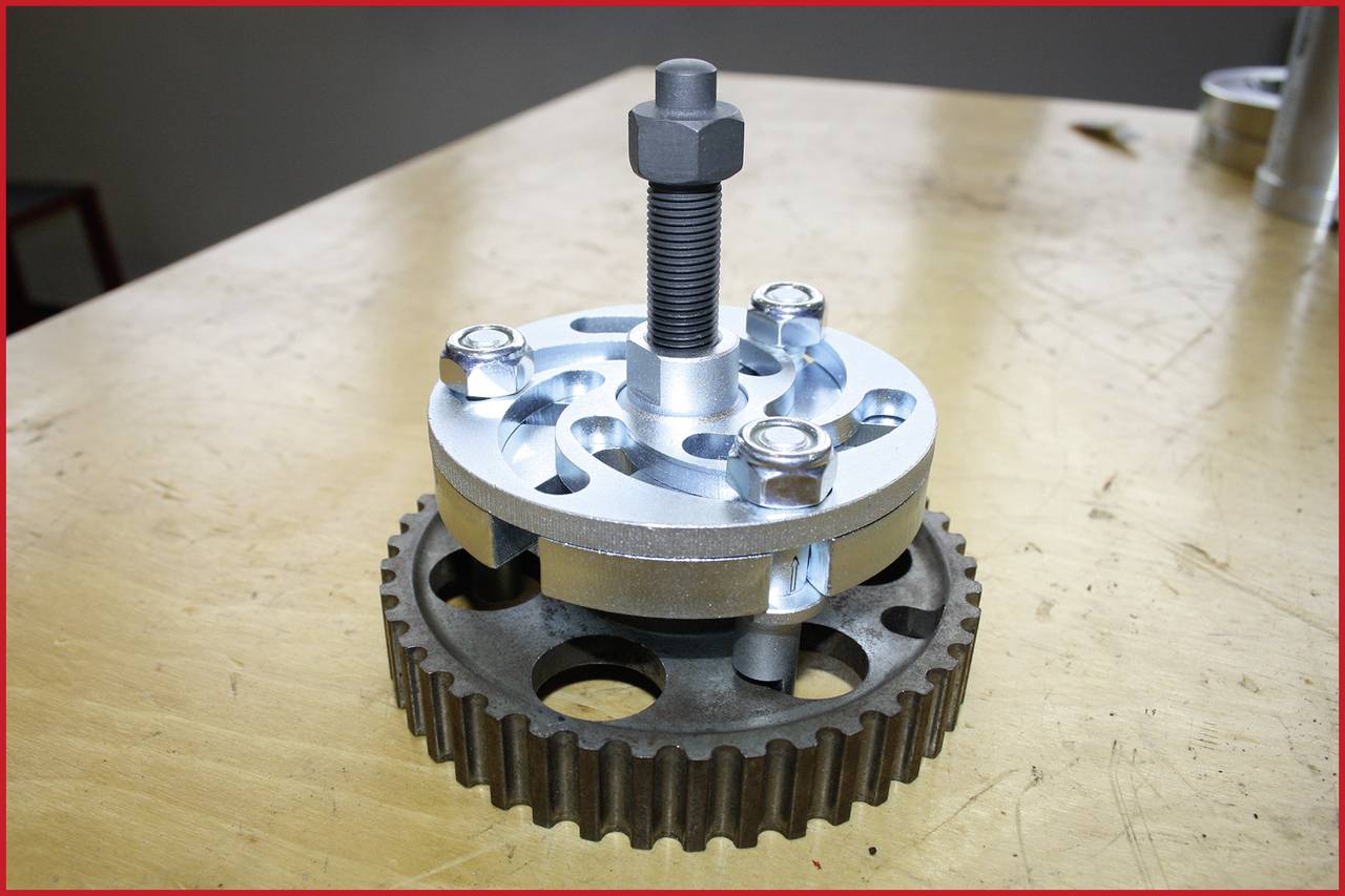 Ein Zahnrad auf einem Holztisch, darüber eine Spezialvorrichtung mit Schrauben. Mechanisches Werkzeug für technische Anwendungen.