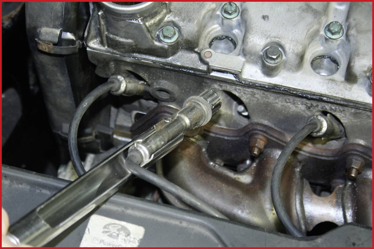 Zündkerze wird aus einem Motorblock entfernt, sichtbar sind Drähte und Metallkomponenten. Fokus auf Reparation oder Wartung im Automobilbereich.