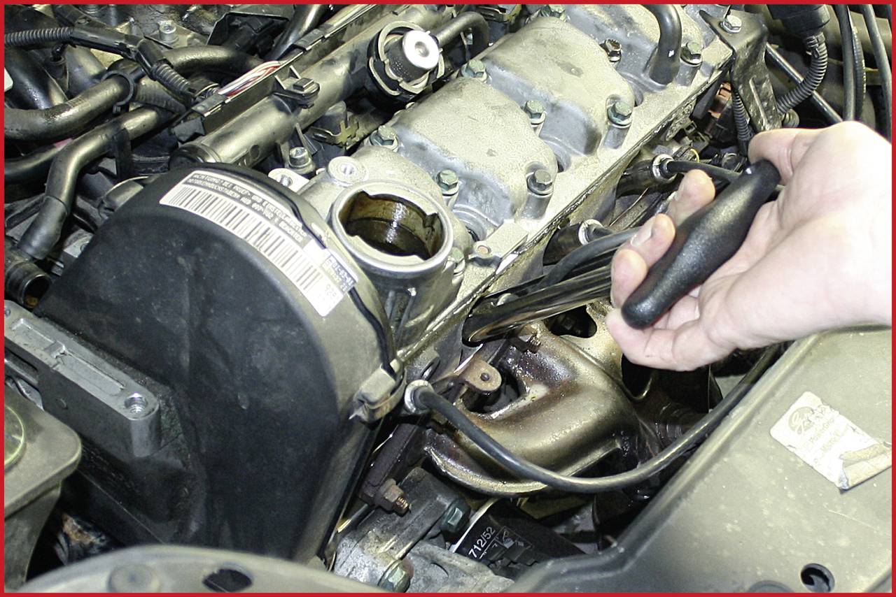 Eine Hand repariert mit Werkzeug einen Motor in einem Auto. Sichtbare Kabel und Motorenteile umgeben die Hauptkomponente.