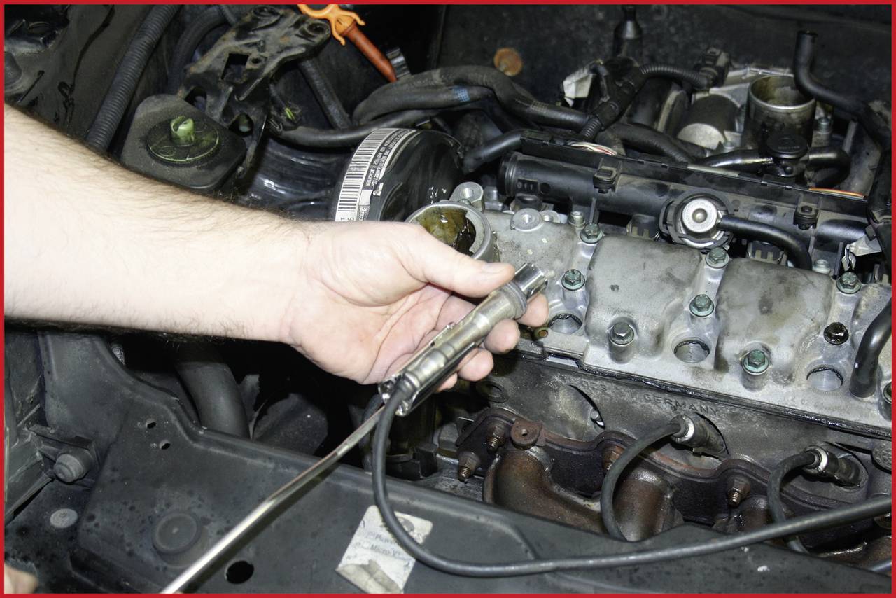 Ein Mechaniker hält eine Zündkerze vor einem geöffneten Motorblock, umgeben von verschiedenen Autoteilen und Werkzeugen.