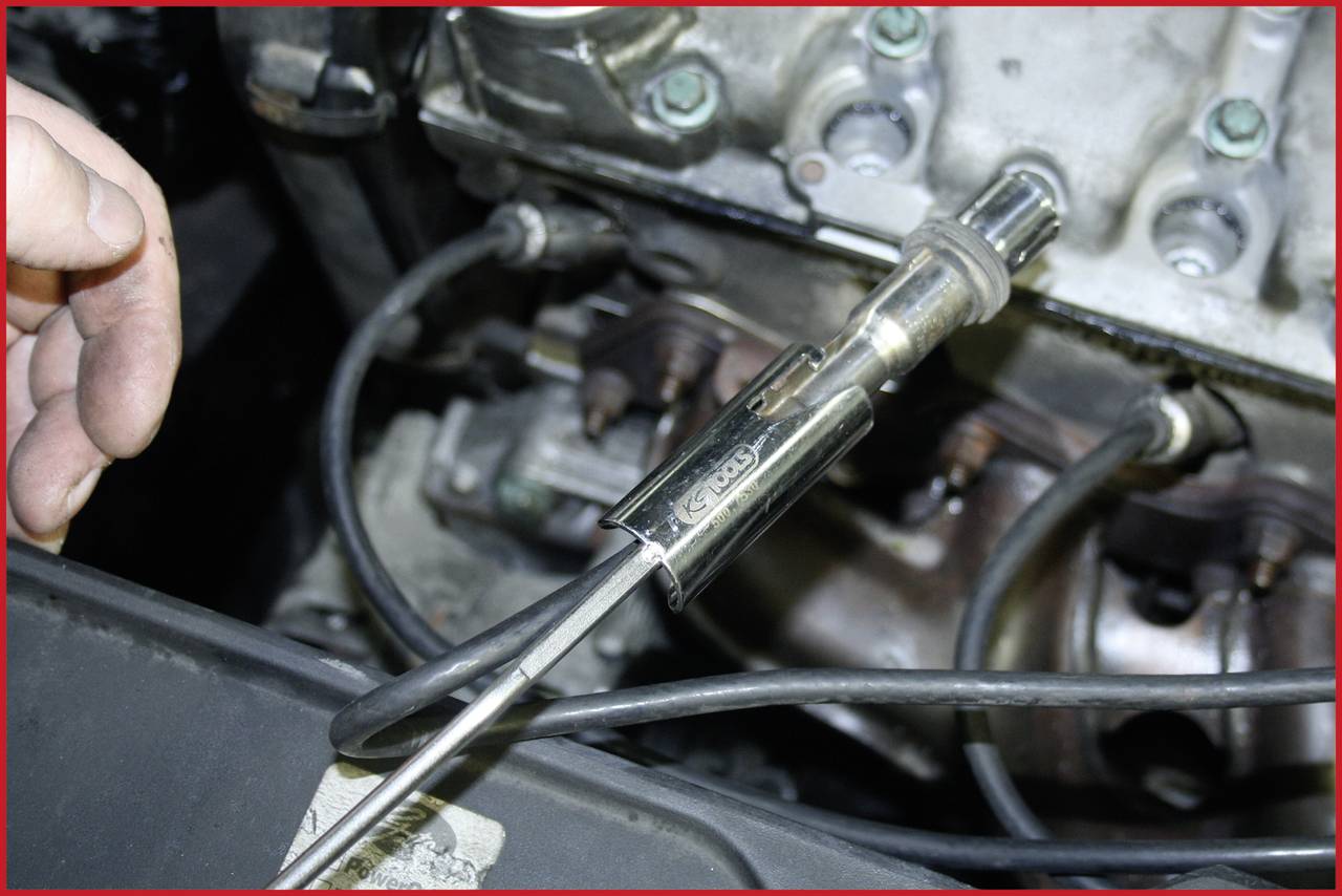 Hand hält eine Lambdasonde vor einem Motor. Die Sonde misst den Sauerstoffgehalt im Abgas und wird zur Regelung des Motors verwendet.