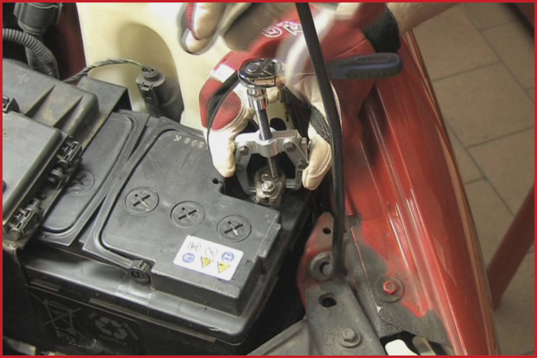 Eine Person mit Handschuhen zieht einen Batteriepol-Abzieher an der Autobatterie an.