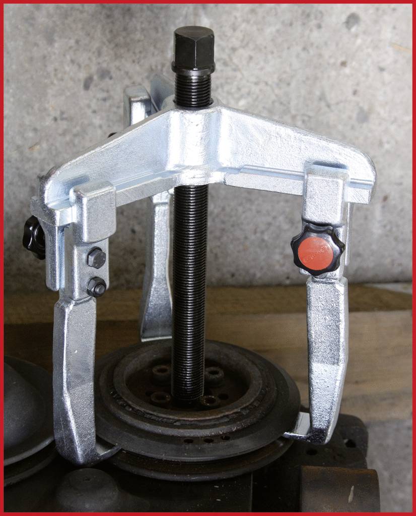 Ein dreibeiniger Abzieher zieht ein Lager von einer Welle. Werkstattumgebung im Hintergrund. Hauptbestandteil ist der Mechanismus des Abziehers.