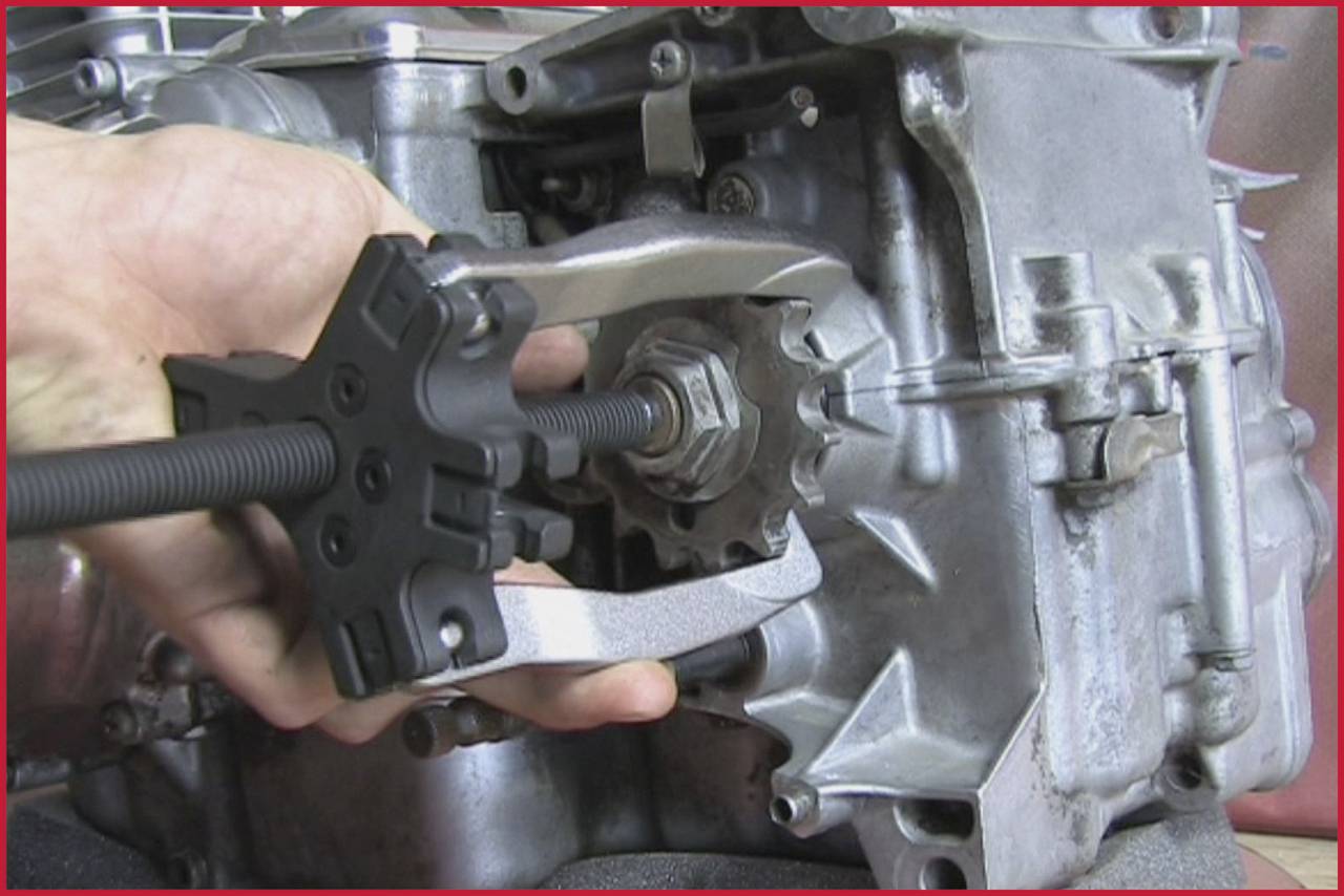 Eine Person verwendet einen Abzieher, um ein Zahnrad von einem Motor zu lösen. Der Motor ist teilweise freigelegt.