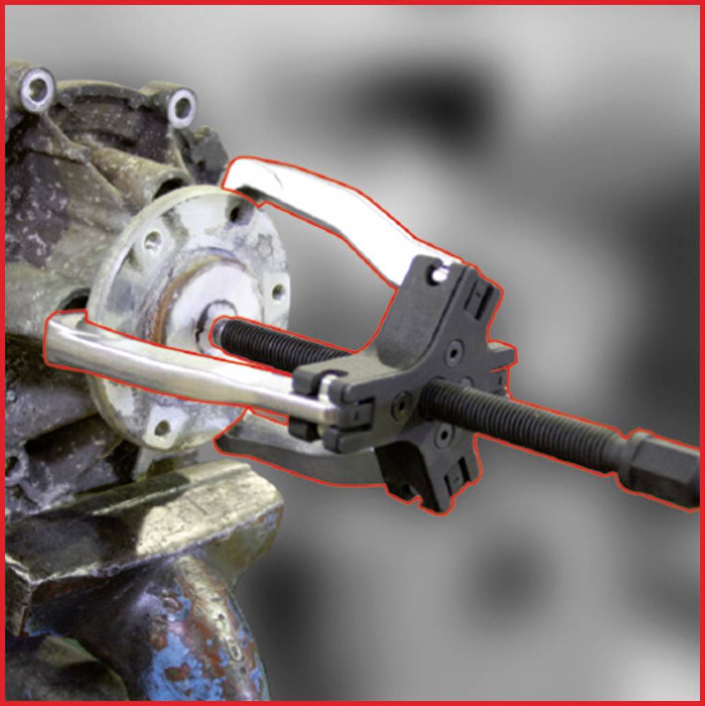 Ein Abzieher entfernt ein Teil von einer Metallmaschine. Der Abzieher hat zwei Arme und ist schwarz. Im Hintergrund verschwommenes, metallisches Gerät.