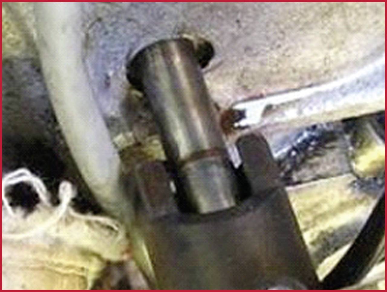 Ein Metallstift oder Bolzen ist in eine Metallhalterung eingesetzt. Umgebung zeigt Schläuche oder Kabel, möglicherweise technische Umgebung.