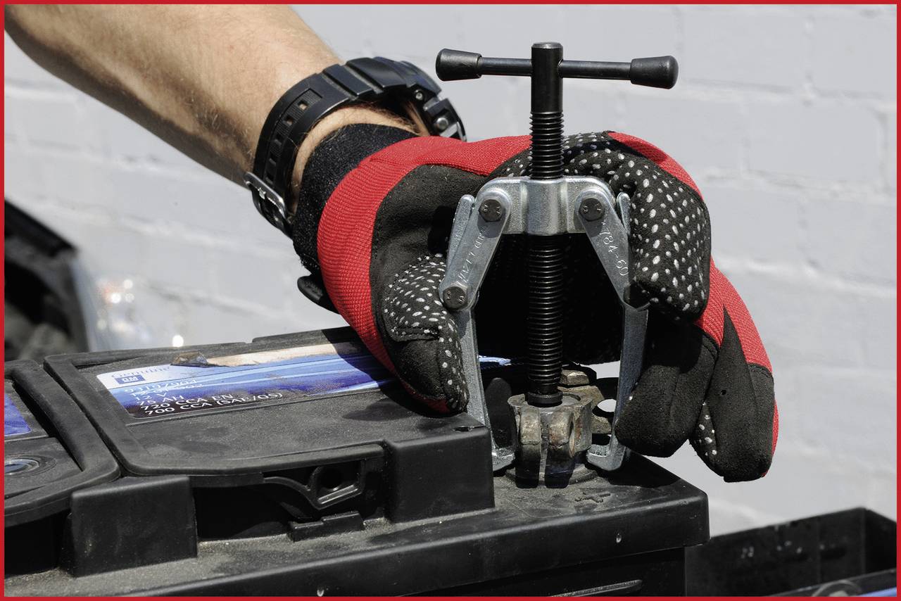 Ein Mechaniker entfernt mit einem Abzieher vorsichtig eine Batteriepolklemme, während er Handschuhe trägt.