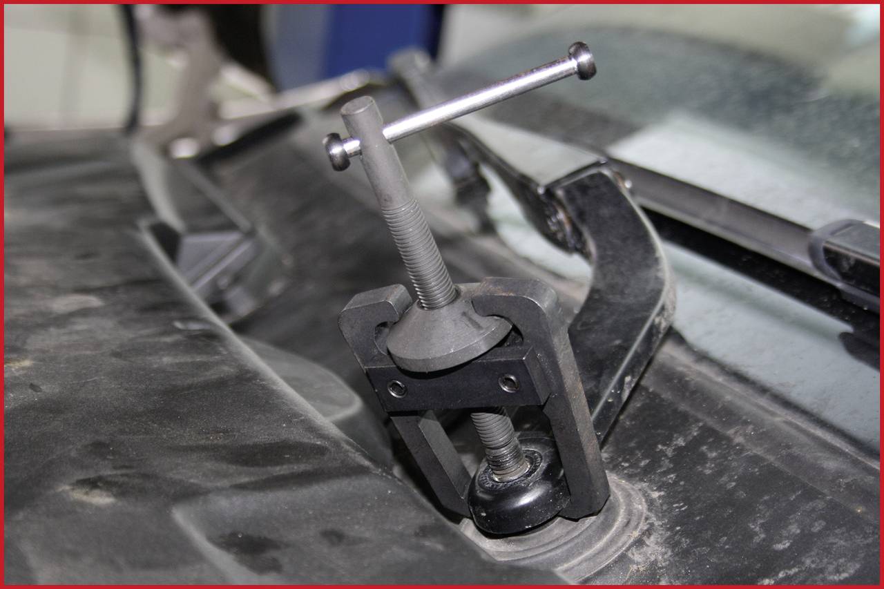 Ein Abzieher-Werkzeug ist auf einem Kugelgelenk angebracht, um es zu entfernen. Das Werkzeug ist auf einem staubigen Autoteil montiert.